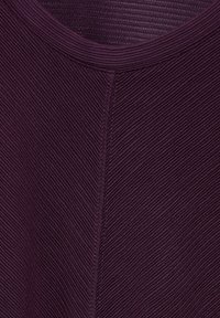 Dunkellila Textil mit geripptem Muster, mit Rundhalsausschnitt und vertikalen Nahtdetails. Keine weiteren Muster oder Hardware sichtbar.