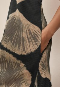 Tissu noir avec un motif de vagues texturé, mettant en vedette de grandes feuilles beiges. Comprend des poches latérales, soulignant le design unique.