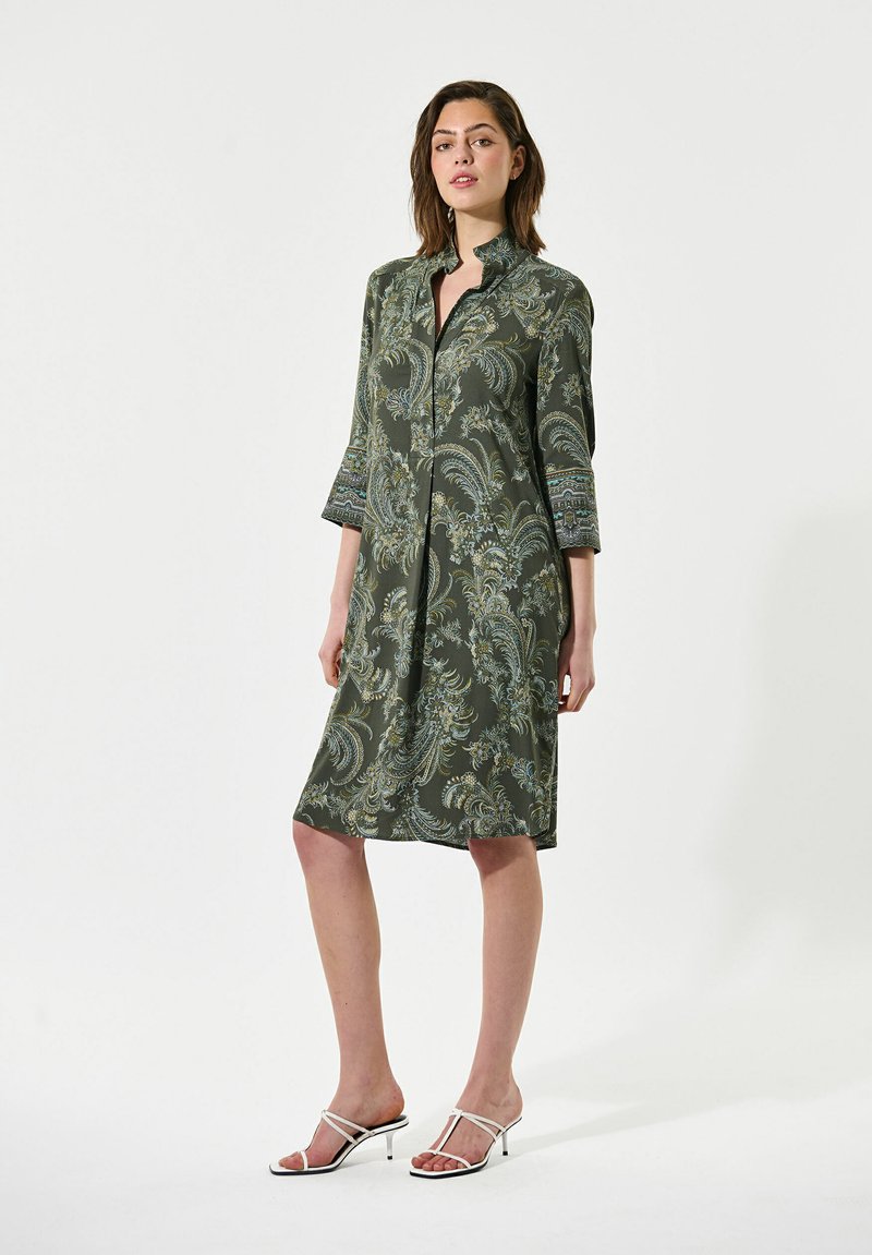 Grün gemustertes Kleid mit langen Ärmeln, Knopfverschluss und knielanger Schnittform. Verfügt über dekorative Manschetten und subtile Blumenmuster.