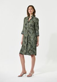 Abito verde realizzato in tessuto leggero, con un motivo paisley, maniche 3/4 e apertura frontale con bottoni. Abbinerà a sandali con tacco bianchi.