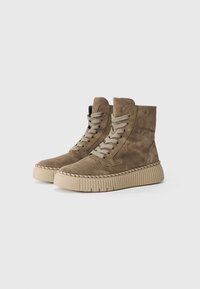 Bottines en suede marron avec une finition texturée, dotées de semelles en caoutchouc beige et de lacets gris. Bout arrondi et détails cousus à la semelle.