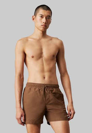 Brune svømmeshorts med elastisk talje og snor, der har en sidelomme og en glat tekstur, båret af en torso.