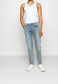 Ljusblå denimjeans med slim fit, med slitningar och urtvättade detaljer. Matchas med en vit linne och vita sneakers.