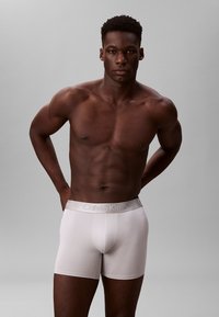 Bóxer de algodón blanco con una suave y elástica cinturilla de Calvin Klein. Textura lisa y diseño ajustado. El modelo posa con los brazos a los lados.