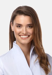 Blouse col bleu clair avec une texture lisse. Cheveux longs, bruns et ondulés. Le sujet a un fond neutre et un large sourire.