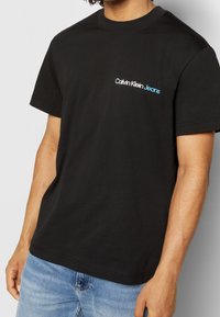 Černé bavlněné tričko s krátkým rukávem, kulatým výstřihem a malým modrým logem "Calvin Klein Jeans" na hrudi.