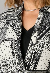 Camicia a righe in bianco e nero caratterizzata da una varietà di design geometrici, con colletto, bottoni e una superficie liscia.