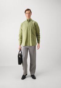 Camicia verde chiaro con bottoni, pantaloni grigi, scarpe nere e una borsa nera. La camicia presenta un colletto e chiusura a bottoni.