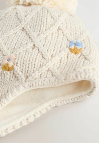 Krēmīgi adīta ziemas cepure ar dimanta rakstu, mazām izšūtām puķītēm, vilnas oderi un pom-pom augšpusē.