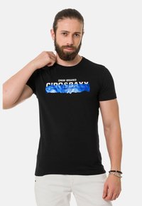 Schwarzes Baumwoll-T-Shirt mit kurzen Ärmeln. Auf der Vorderseite befindet sich ein grafischer Text in Weiß und Blau mit der Aufschrift "DNM BRAND CIRCUS BAXY." Einfaches, tailliertes Design.