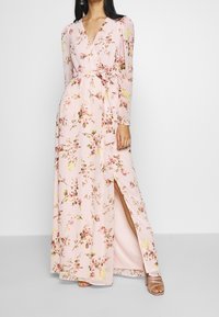 Abito maxi con maniche lunghe, in tessuto rosa decorato con motivi floreali, scollatura a V, vita con cintura e uno spacco laterale per un tocco in più.