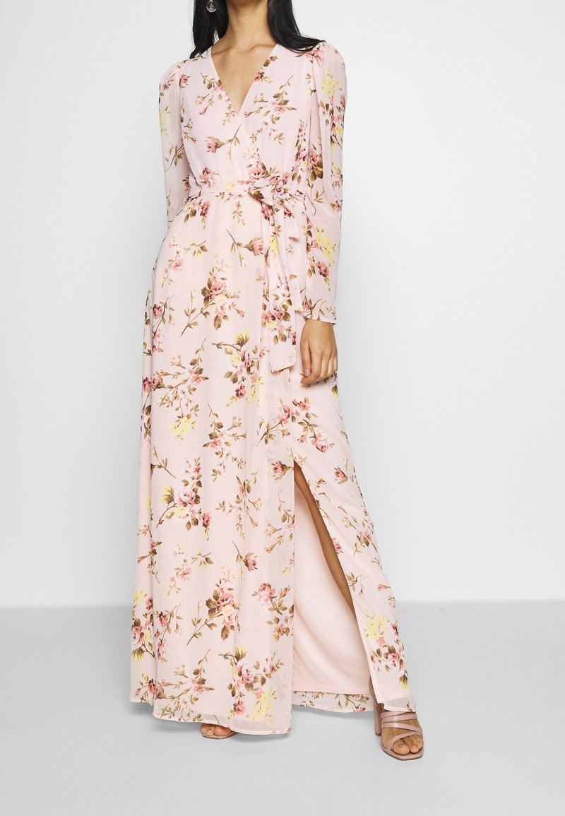 Abito maxi con maniche lunghe, in tessuto rosa decorato con motivi floreali, scollatura a V, vita con cintura e uno spacco laterale per un tocco in più.