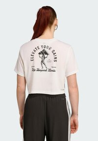 T-shirt blanc court avec un graphique noir et du texte sur le dos. Le texte dit "ÉLEVEZ VOS RÉSULTATS" et "Soulevez au-delà des limites."