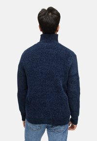 Marineblå sweater med høj krave, ribbet struktur og mønstrede strikkede ærmer. Fremstillet af tykt, varmt materiale, ideel til koldt vejr.