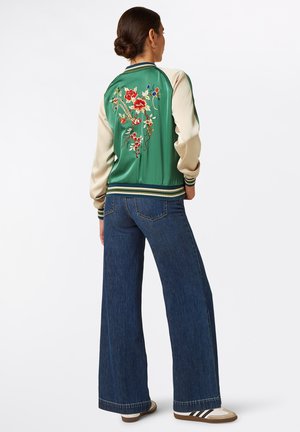 Zielona satynowa kurtka typu bomber z kościanymi rękawami, ozdobiona kwiatową haftem na plecach. Połączona z szerokimi, niebieskimi jeansami i sneakersami.