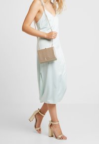 Abito in satin azzurro chiaro con una fessura laterale, abbinato a una borsa a mano strutturata in metallo dorato e sandali con tacco alto color oro chiaro. Borsa con tracolla a catena.