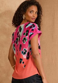 Flerfärgad kortärmad topp med ett livligt djurtryck i rosa, blått och svart på en korallbakgrund med en avslappnad passform.