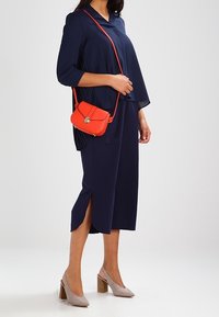 Top blu navy sfuso con maniche corte, abbinato a culotte blu navy. Presenta una borsa arancione a tracolla e scarpe con tacco beige, creando un look stratificato.