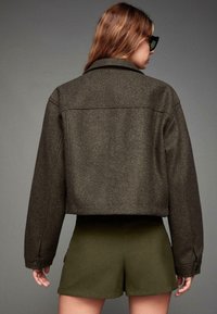 Bruine wolmix cropped jack met een puntige kraag, knoopmanchetten en een gestructureerde afwerking, gecombineerd met olijfgroene shorts.