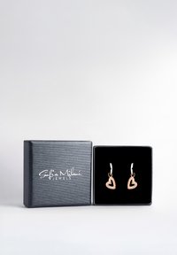 Orecchini a forma di cuore in tono oro con accenti di pietre preziose trasparenti, esposti in una scatola per gioielli nera imbottita con logo argento su una superficie testurizzata.
