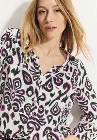 Vit blus med ett svart och fuchsia abstrakt mönster, rund halsringning och långa ärmar, tillverkad i ett lätt material.