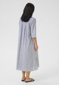 Rochie lungă căptușită în carouri gri și alb, cu mâneci trei sferturi, croi lejer, slituri laterale și material din bumbac ușor.