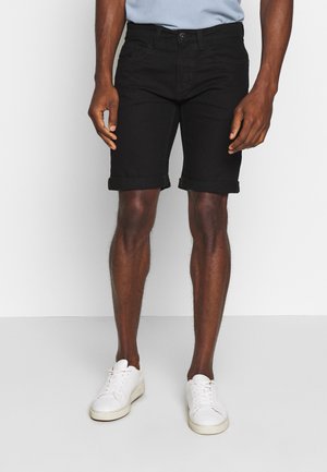 Shorts de mezclilla negra con dobladillo enrollado, con un diseño clásico de cinco bolsillos. Combinados con zapatillas blancas. Enfoque en el corte y la forma.