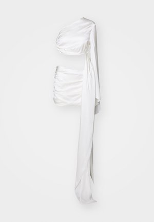 Λευκή σατέν τοπ, ένα ώμου με draped σχέδιο. Διαθέτει ραφές και μια μακριά, ρέουσα ζώνη. Λείο υφή, κομψή σιλουέτα.