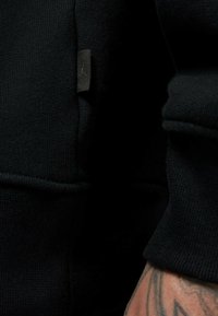 Felpa nera realizzata in tessuto testurizzato, dotata di una piccola etichetta nera con logo, polsini e orlo a costine e una vestibilità aderente.