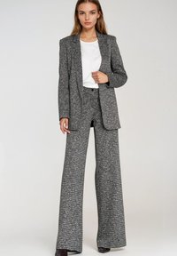 Szary i czarny garnitur w pepitkę z szerokimi spodniami o nogawkach i dopasowaną marynarką, zestawiony z białym topem. Gładka faktura i usztywniony fason.