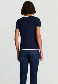 Marineblaues T-Shirt mit kurzen Ärmeln und kontrastierendem weißem Saum am Ausschnitt und an den Ärmeln. Weicher Stoff, figurbetonte Form und minimalistisches Design.