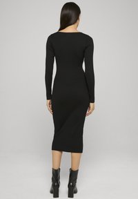 Robe noire en maille côtelée avec une silhouette ajustée, manches longues et encolure dégagée, associée à des bottines noires. Design simple et élégant.