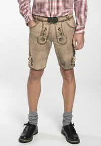 Beige leren shorts met geborduurde bloemmotieven, voorzakken en metalen knopen. Gepaard met grijze opgerolde sokken en zwarte schoenen.