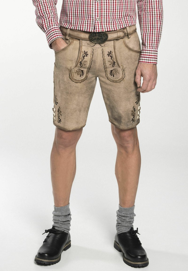 Beige leren shorts met geborduurde bloemmotieven, voorzakken en metalen knopen. Gepaard met grijze opgerolde sokken en zwarte schoenen.
