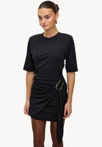 Robe noire à manches courtes, avec un design froncé et des accents en métal doré. Confectionnée en tissu doux et extensible, avec un détail de ceinture à la taille.