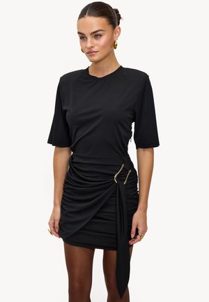 Robe noire à manches courtes, avec un design froncé et des accents en métal doré. Confectionnée en tissu doux et extensible, avec un détail de ceinture à la taille.