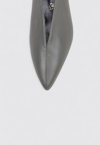 Pointed-toe pump in grey leather with a sleek upper design, featuring a central cutout and smooth texture. Stitched detailing along the edges.