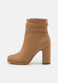 Bottes chelsea en daim marron clair avec un design souple et froissé et un talon haut et épais. Bout arrondi et texture lisse avec des détails de couture minimaux.