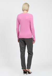 Suéter de manga larga color rosa claro con un cuello acanalado, combinado con pantalones gris ajustados. La tela parece suave y lisa, con una silueta ajustada.