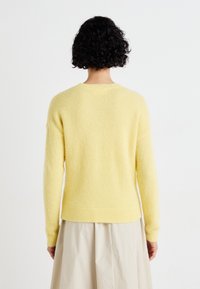 Yellow knitted sweater with a textured, fluffy fabric. Features a crew neckline and ribbed cuffs, designed with a relaxed fit and dropped shoulders.