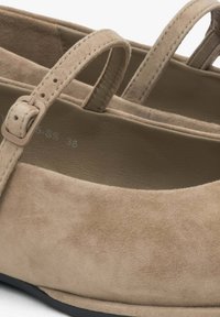 Beżowe zamszowe buty z okrągłym noskiem i pojedynczym paskiem z klamrą. Podeszwa jest płaska i fakturowana dla lepszego uchwytu.