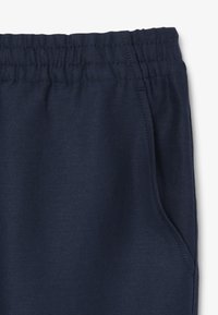 Joggers de tela elástica en azul marino, con cintura elástica y bolsillo lateral, que presentan una textura suave y un leve brillo.