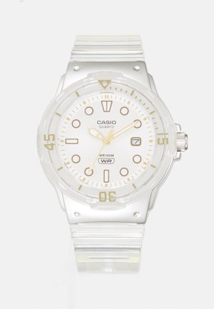 Montre-bracelet en plastique transparent Casio avec cadran blanc, marquages dorés, fenêtre de date et résistance à l'eau jusqu'à 100 mètres.