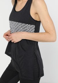 Černý sportovní top bez rukávů s geometrickým bílým vzorem na hrudi, kulatým výstřihem a bočními rozparky pro odvětrávání.