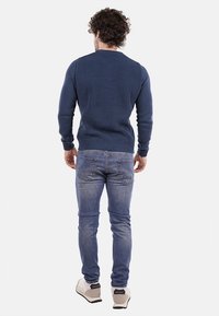 Maglione lavorato a maglia blu navy con texture a coste, design aderente e maniche lunghe, abbinato a jeans blu chiaro e sneakers beige.