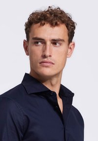 Marineblauw overhemd met knoopsluiting, voorzien van een klassieke kraag en een gladde textuur. Decoratieve knopen zichtbaar, het aansluitende ontwerp benadrukt de schouders en borst.