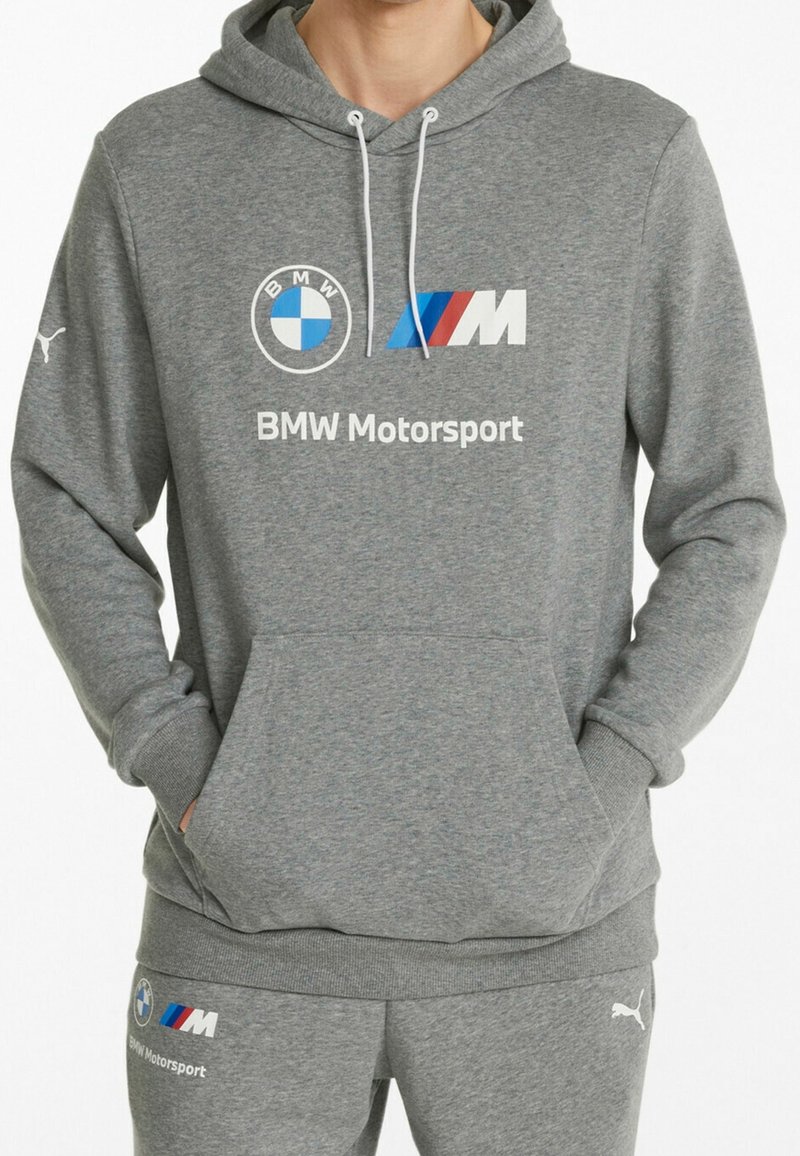 Grijze hoodie van zacht materiaal met een voorkantzak. Heeft BMW en Puma logo's, de tekst "BMW Motorsport" en witte trekkoorden.