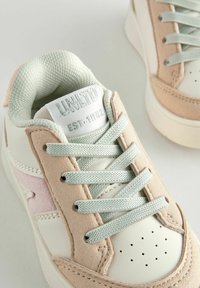 Sneakers med en hvid læderbund, lyserøde ruskindselementer og lys grå snørebånd. Tekstureret tunge med logo; perforeringer for åndbarhed.