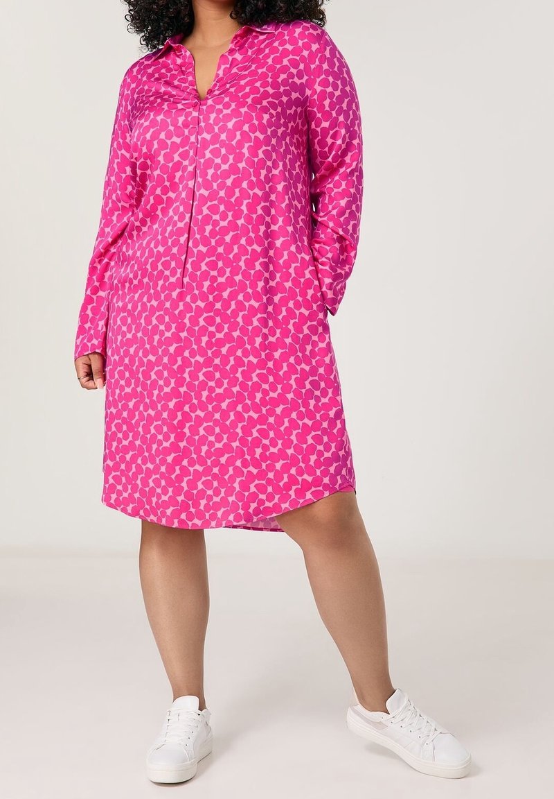 Robe à manches longues, rose vif avec un col rond, présentant un motif répété de petites formes. Tissu lisse ; longueur au genou.