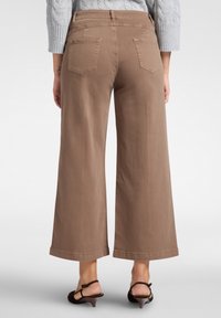 Ruskeat leveät housut, joissa on sileä pinta, kaksi takataskua ja suora helma. Yhdistetty harmaaseen neulepaitaan ja korkokenkiin.